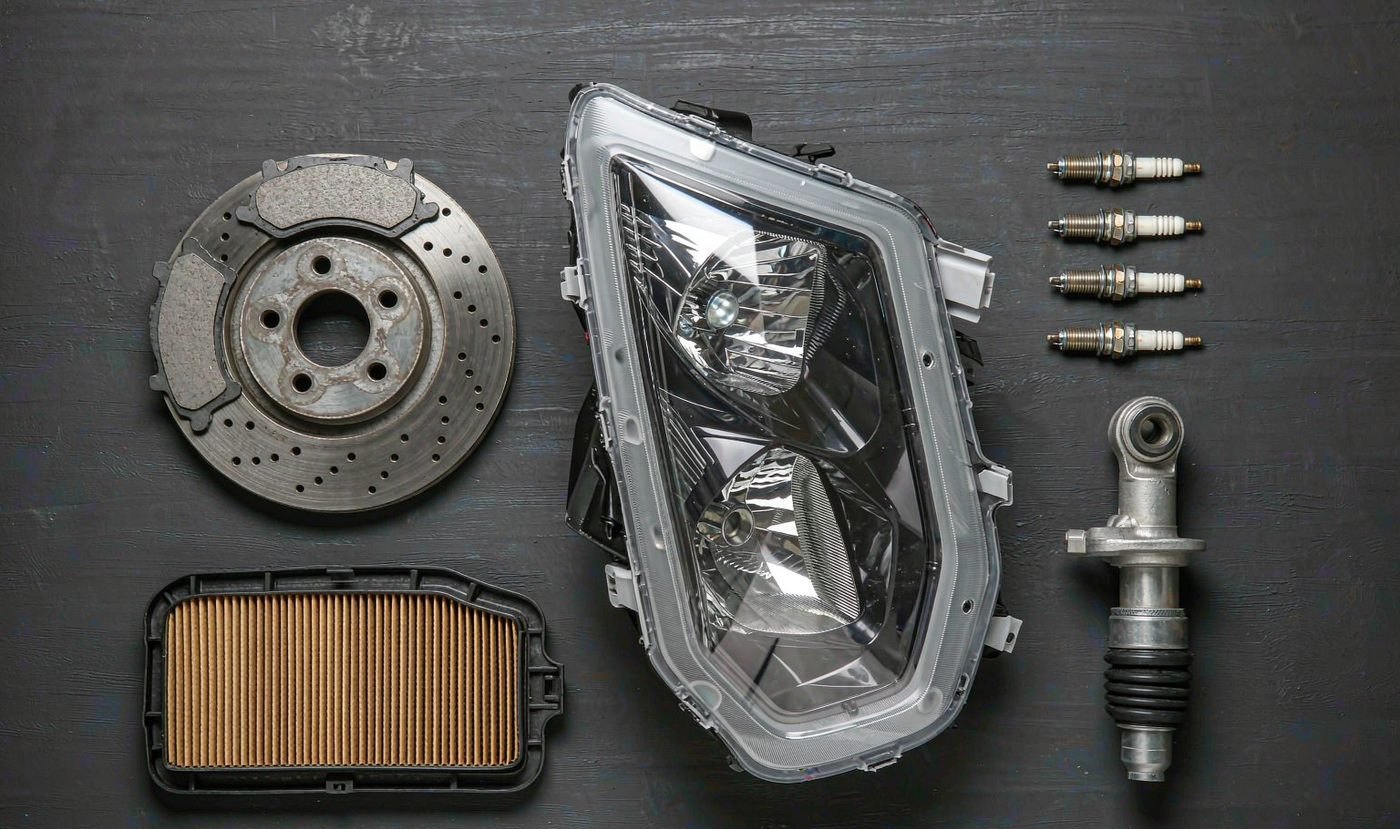 Automotive parts laid out flat: brake disc, headlamp, air filter, spark plugs and shock absorber